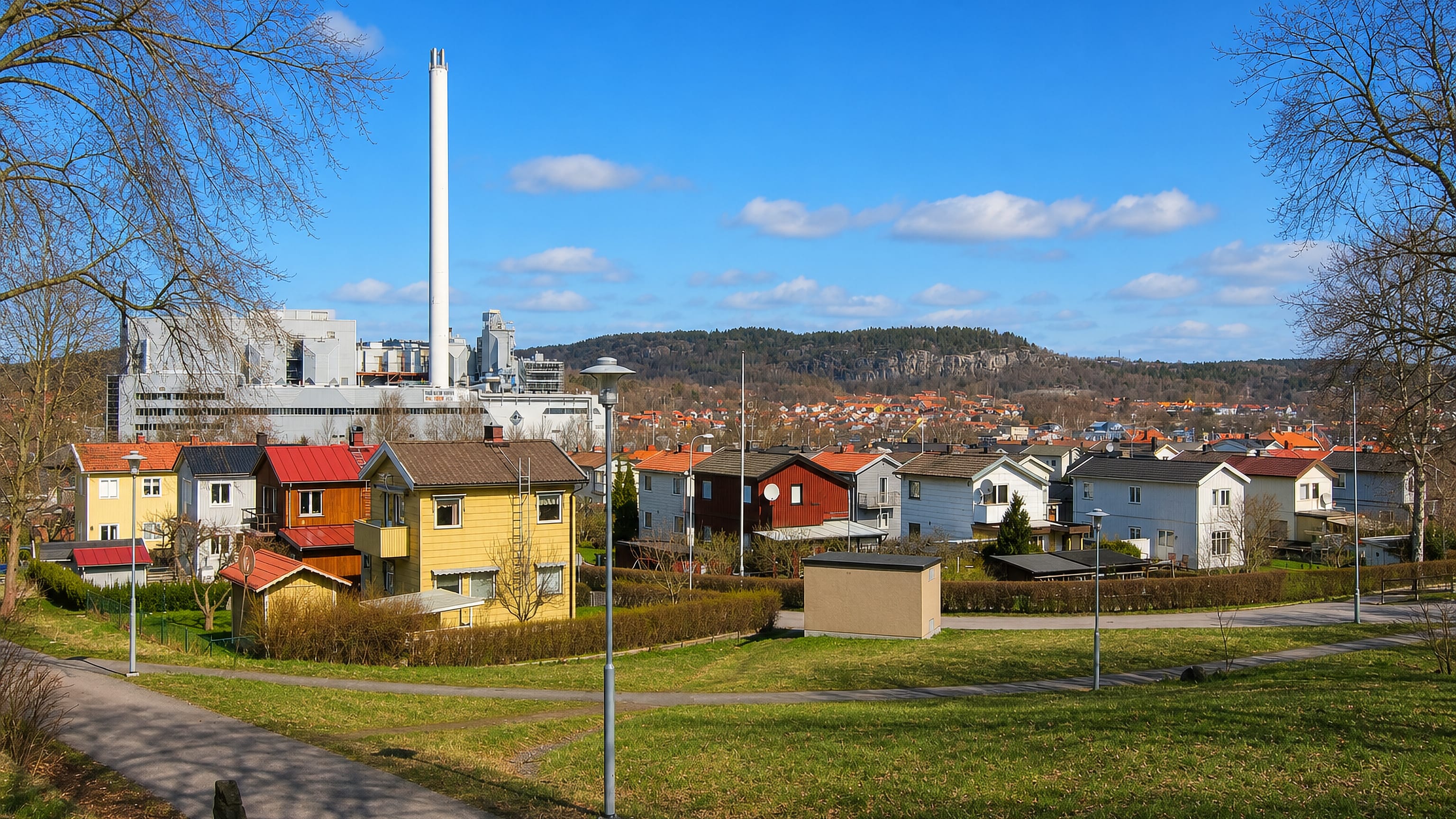 Wooden houses and a tall industrial chimney below rocky wooded hills in Sävenäs, Gothenburg.