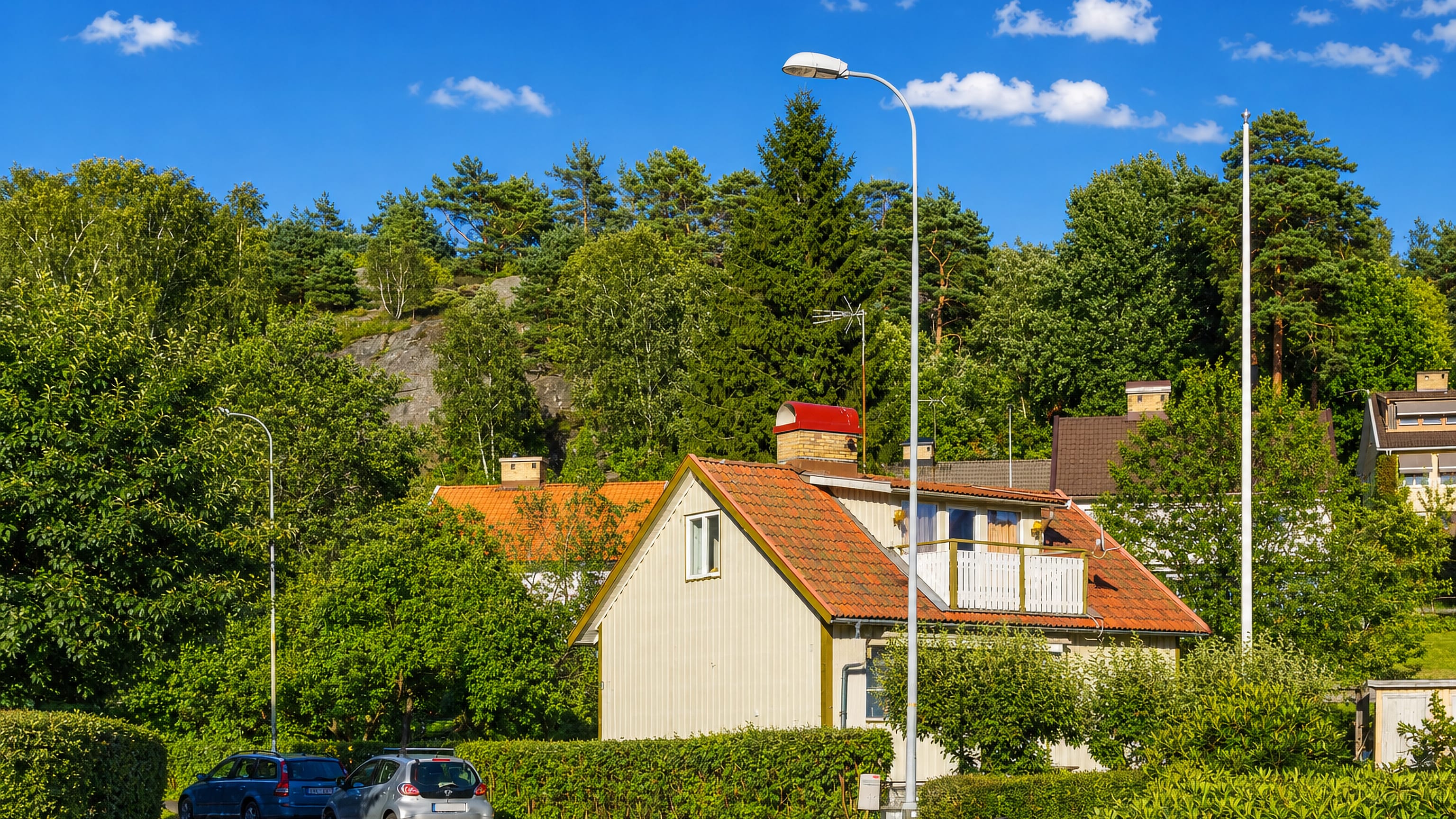 Wooden houses beneath a rocky wooded ridge on a quiet street in Tolered, Gothenburg