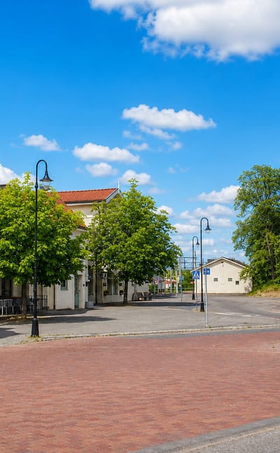 White gabled station building and brick-paved square with a bus shelter in Herrljunga, Sweden.
