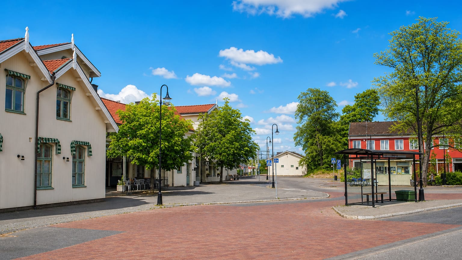 White gabled station building and brick-paved square with a bus shelter in Herrljunga, Sweden.