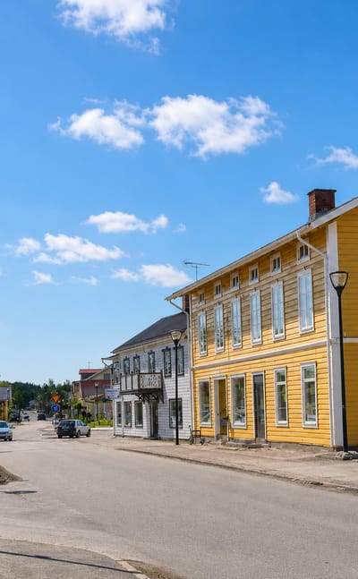 Yellow wooden building and Swedish flags along Hova's sunny main street, Sweden.