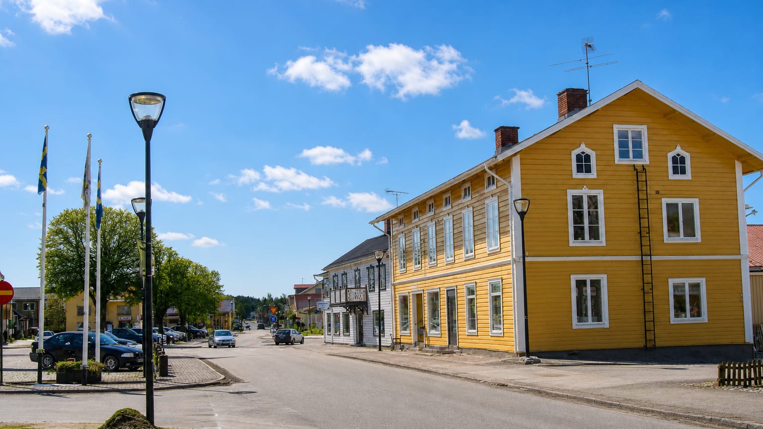 Yellow wooden building and Swedish flags along Hova's sunny main street, Sweden.