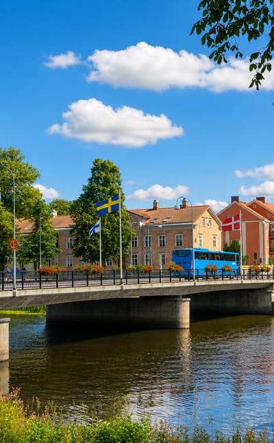 A bridge over the Lidan river in Lidkoeping, with a church spire, riverside houses and Nordic flags flying.
