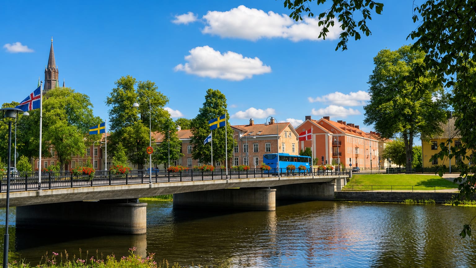 A bridge over the Lidan river in Lidkoeping, with a church spire, riverside houses and Nordic flags flying.
