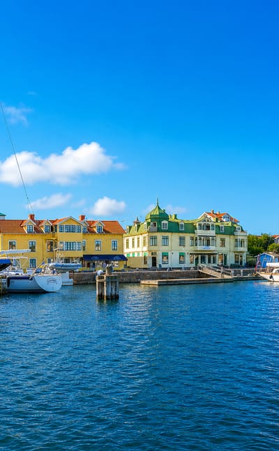 Marstrand harbour in Sweden with moored sailboats, pastel-coloured waterfront houses and Carlsten fortress on the hill behind.