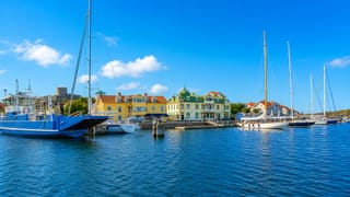 Marstrand harbour in Sweden with moored sailboats, pastel-coloured waterfront houses and Carlsten fortress on the hill behind.
