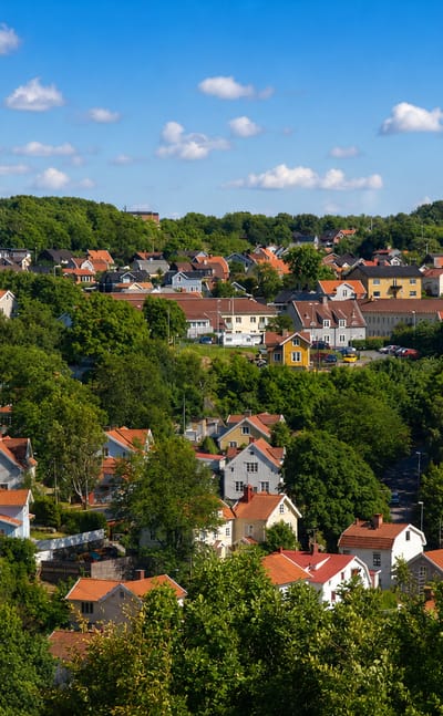 Leafy hillside of red-roofed and yellow wooden houses among dense green trees in Molndal, Sweden.