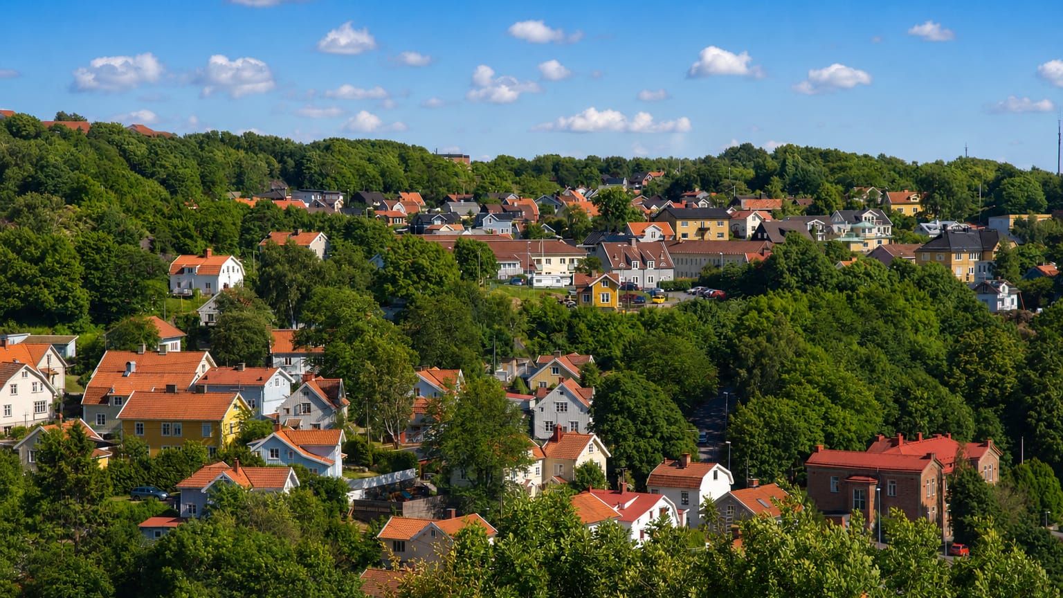 Leafy hillside of red-roofed and yellow wooden houses among dense green trees in Molndal, Sweden.