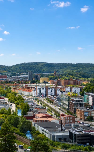 Elevated daytime view of Krokslätt, Sweden: motorway valley, modern apartments, red-brick factories and forested hills.