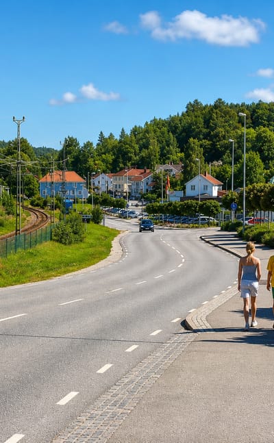 Two people walking along a roadside path beside a railway and houses in Munkedal, Sweden
