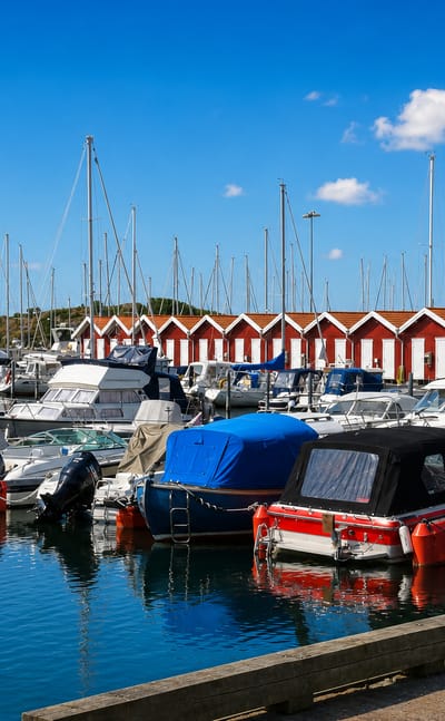 Öckerö marina with moored leisure boats and a row of red-and-white boathouses under a blue sky