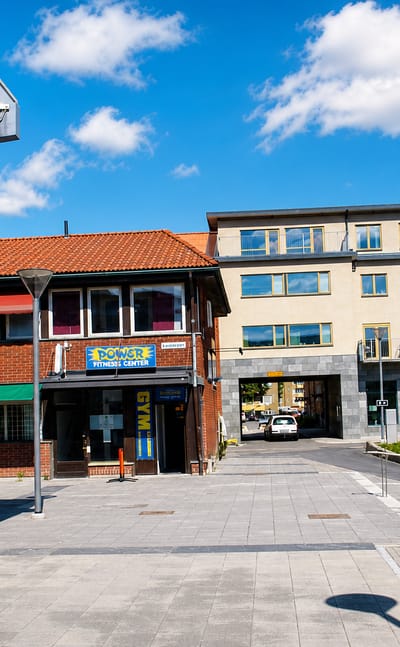 A Partille town-centre plaza with shopfronts including a fitness centre and the Partillebo building under a blue sky.