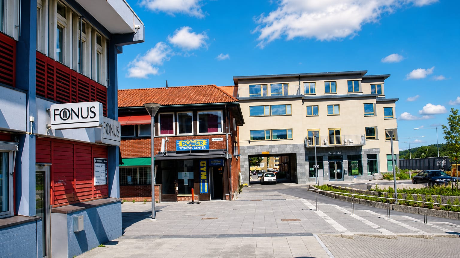 A Partille town-centre plaza with shopfronts including a fitness centre and the Partillebo building under a blue sky.