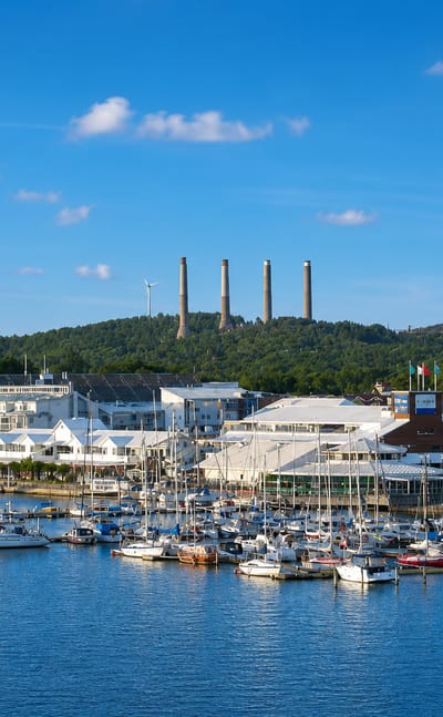 Stenungsund marina full of moored yachts with the town's tall petrochemical chimneys on the wooded hill behind