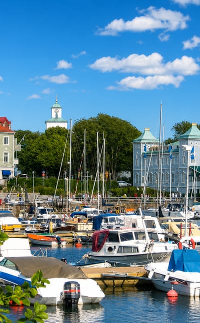 Strömstad's harbour full of boats with the green-domed spa building and old-town rooftops behind under a blue sky.