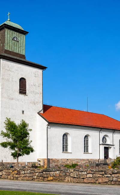 The whitewashed Tanum church with its green copper tower and red-tiled roof beside a stone-walled churchyard in Tanumshede.