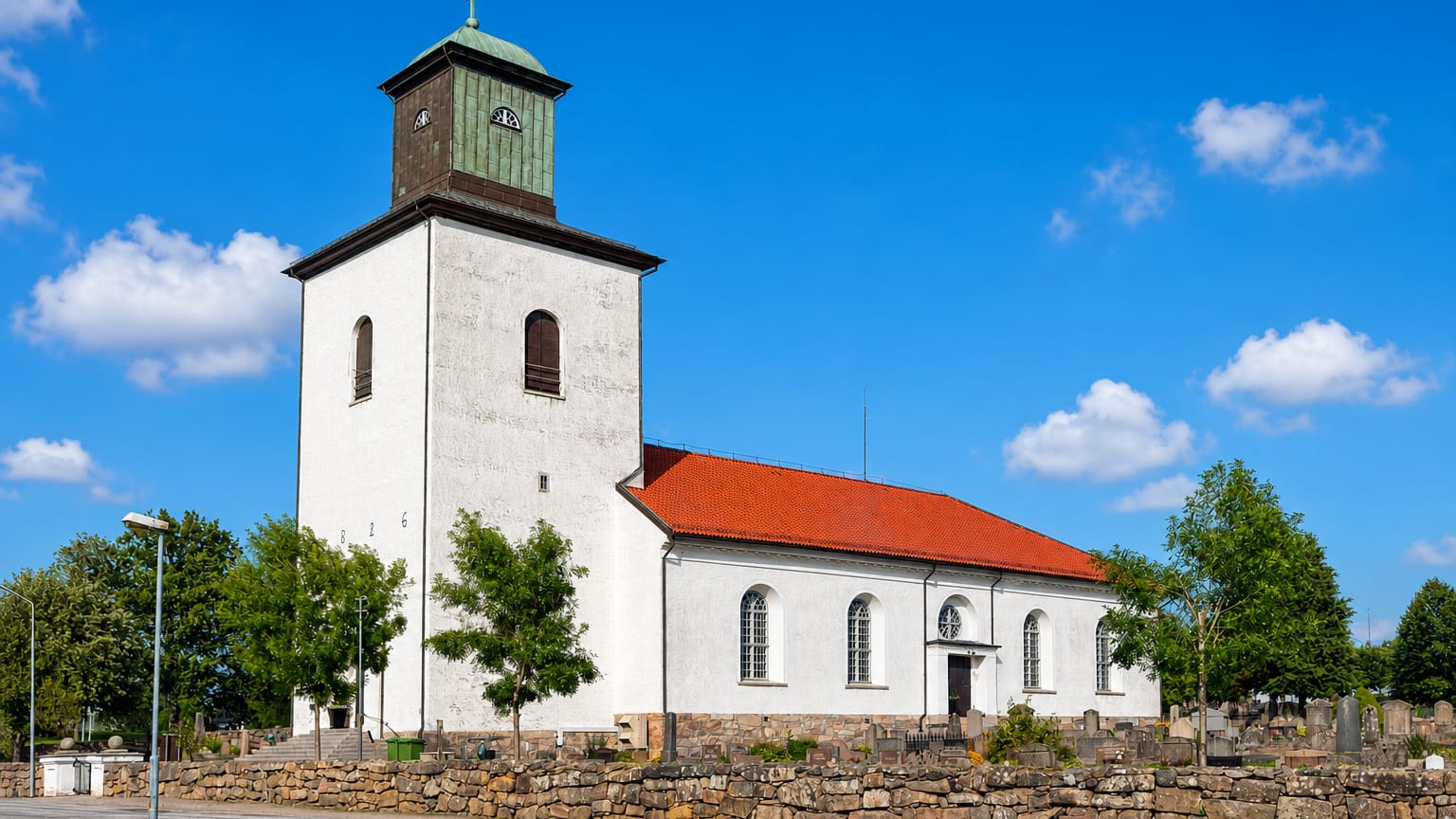 The whitewashed Tanum church with its green copper tower and red-tiled roof beside a stone-walled churchyard in Tanumshede.