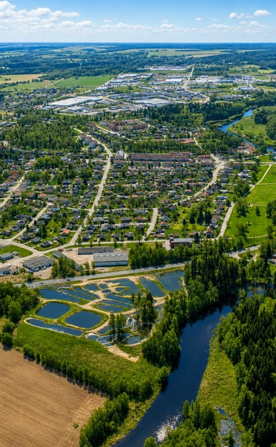 Aerial view of Tibro, Sweden, a small town with a winding river, residential streets and surrounding forest under a blue summer sky.