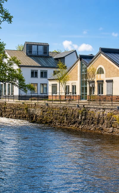 Tidaholm's old industrial mill buildings with arched windows lining the Tidan river beside a weir.
