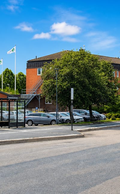 Bus terminal and red-brick office building beside a parking area under blue sky in Tranemo, Sweden.
