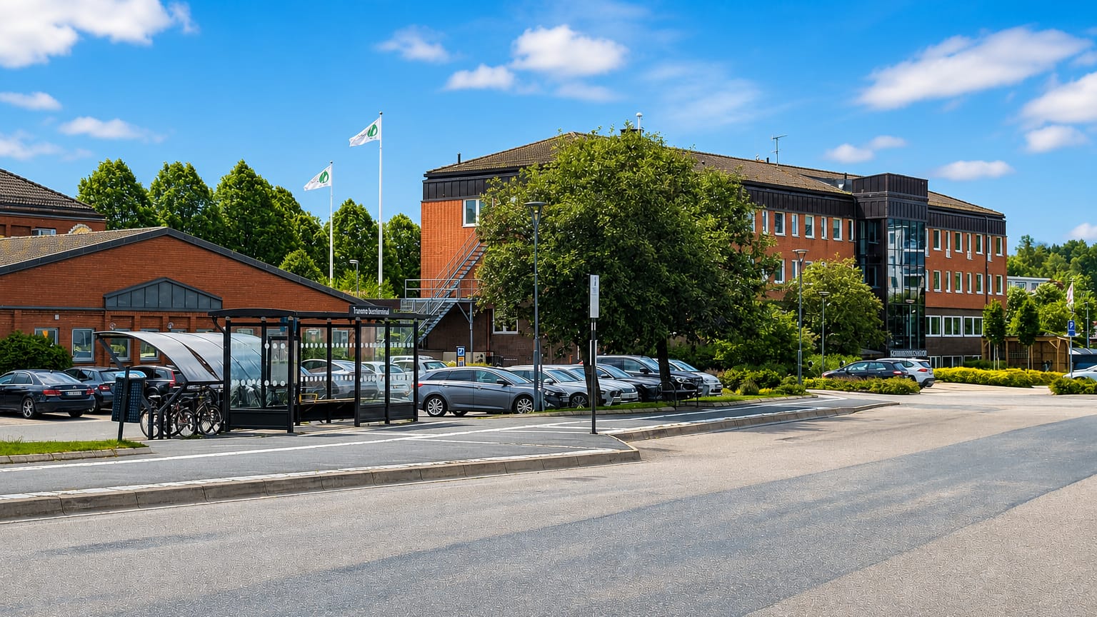 Bus terminal and red-brick office building beside a parking area under blue sky in Tranemo, Sweden.