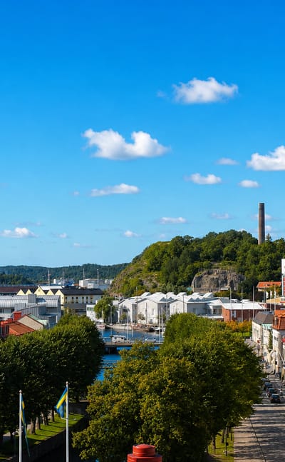 Elevated view over Uddevalla with its harbor cranes, wooded hill and tree-lined avenue below a blue sky