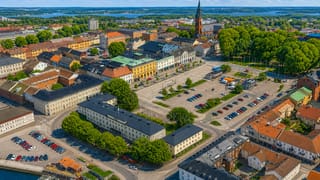 Aerial view of Vänersborg's central square and church spire with the lakeshore and archipelago behind under a blue sky.