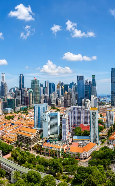 Aerial view of Singapore's central business district skyscrapers rising behind Chinatown shophouse rooftops and a green heritage housing block