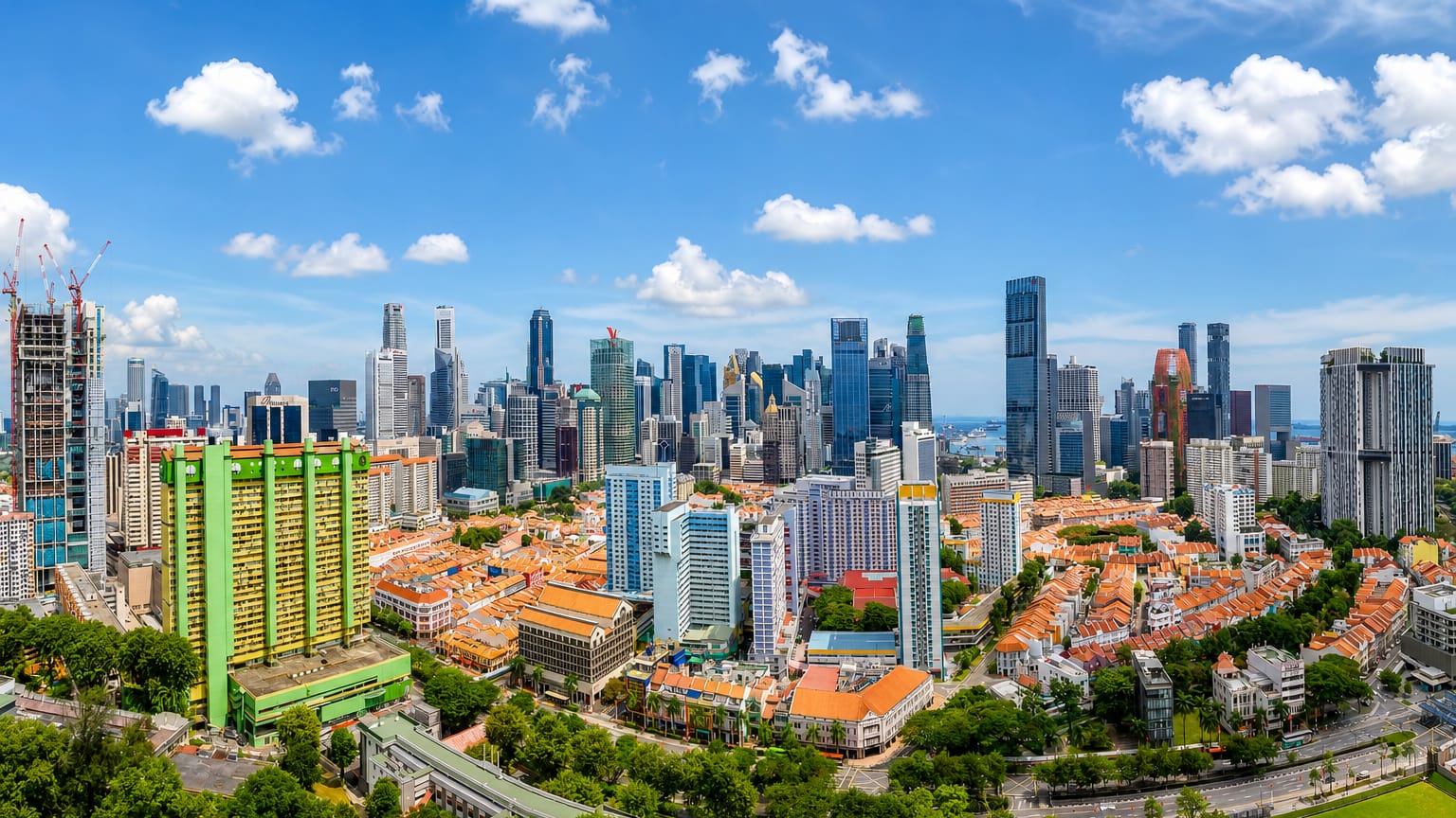 Aerial view of Singapore's central business district skyscrapers rising behind Chinatown shophouse rooftops and a green heritage housing block