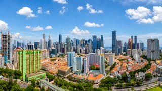 Aerial view of Singapore's central business district skyscrapers rising behind Chinatown shophouse rooftops and a green heritage housing block