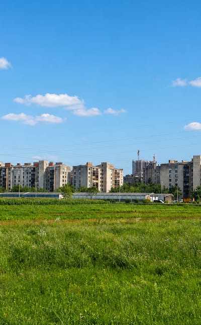 Rows of mid-rise apartment blocks in the Nove Jarše district of Ljubljana behind a green meadow under a blue sky