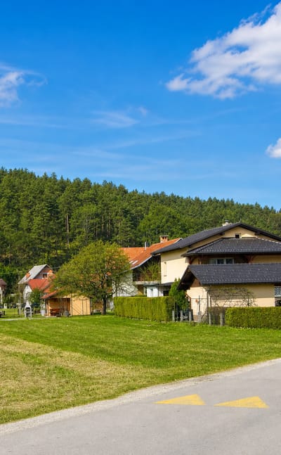 Detached houses and a quiet road below a forested hillside in Podgorica pri Črnučah, a suburban village of Ljubljana