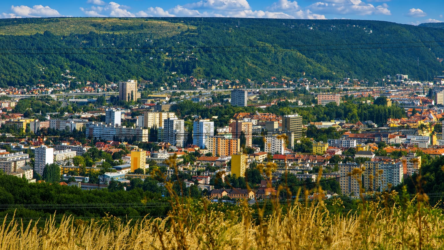 Panorama of Kosice, Slovakia, with residential apartment blocks spread across a valley beneath wooded hills.