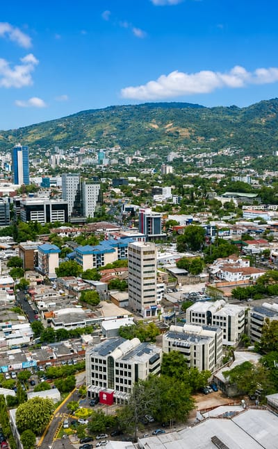 Aerial view of San Salvador spreading below the forested San Salvador Volcano under a blue sky.