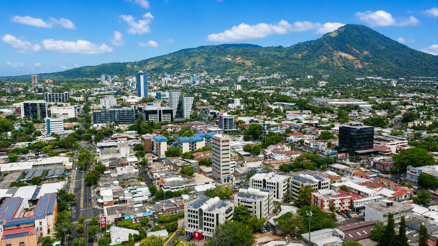 Aerial view of San Salvador spreading below the forested San Salvador Volcano under a blue sky.