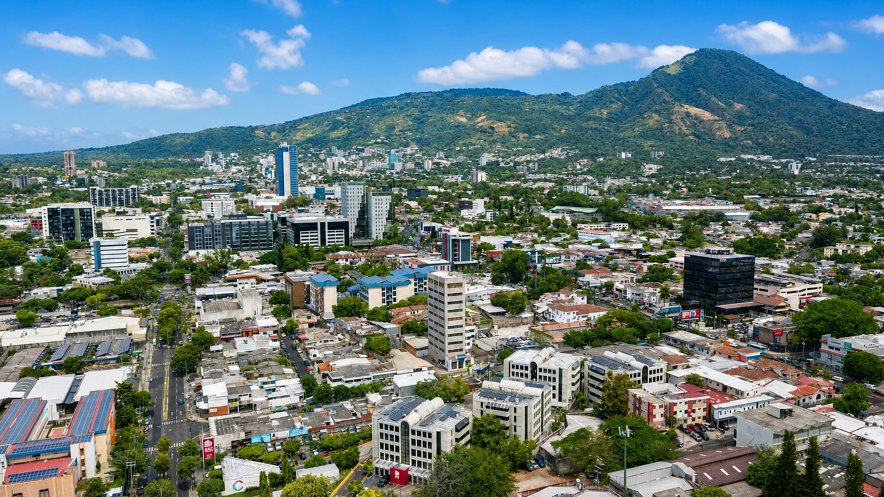 Aerial view of San Salvador spreading below the forested San Salvador Volcano under a blue sky.