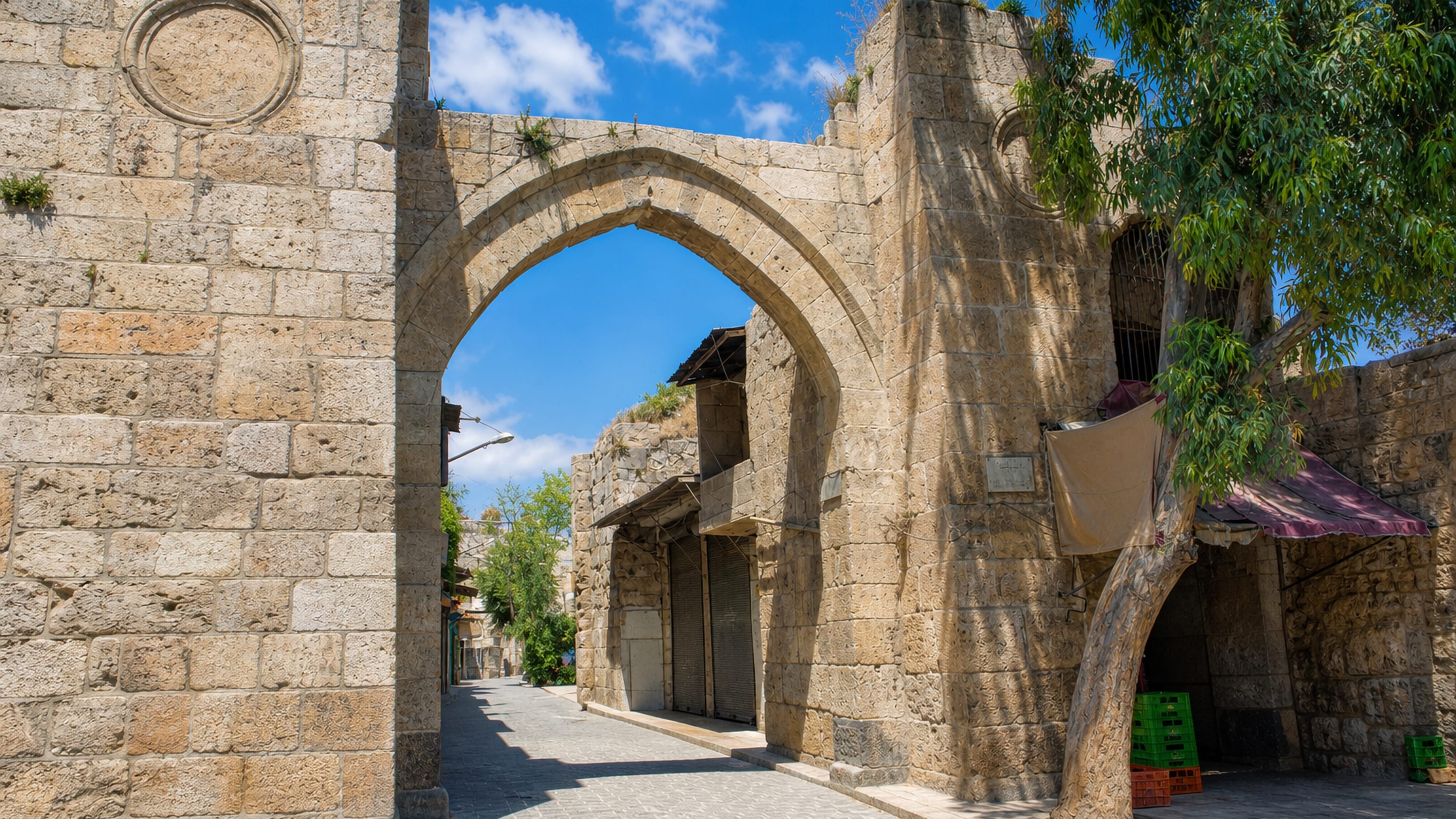 Weathered stone gateway with a pointed arch opening onto an old paved lane at Bab al-Maqam, Aleppo.