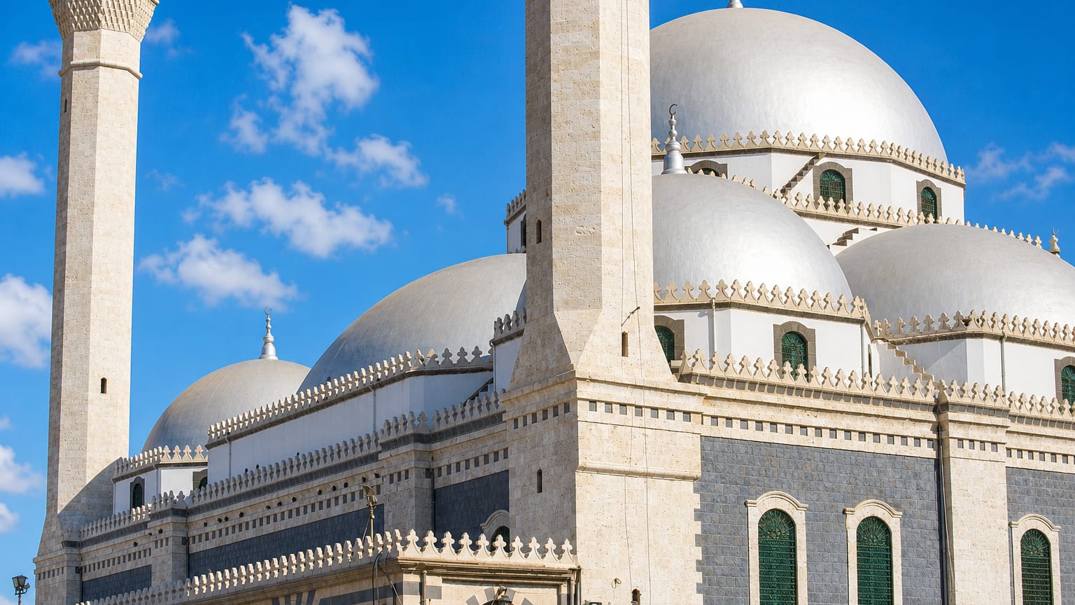White-domed Khalid ibn al-Walid Mosque with its tall minaret under a blue sky in Homs.