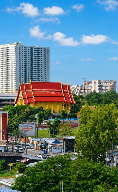 Bang Na district in Bangkok with high-rise apartment towers and a red-roofed Thai temple among greenery