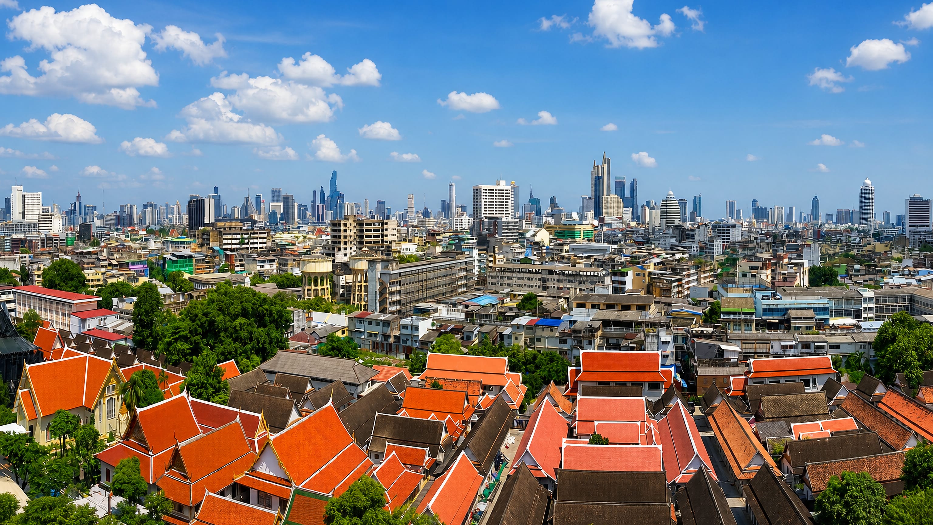 Bangkok's orange-tiled temple roofs in the foreground with the modern high-rise skyline beyond under blue sky.