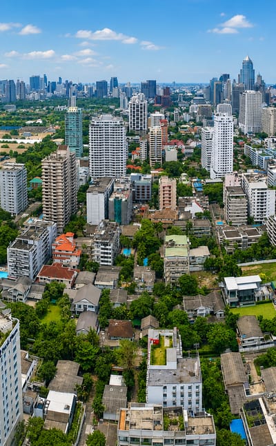 Aerial view of Khlong Toei's dense low-rise blocks with the Bangkok skyline and a lake beyond