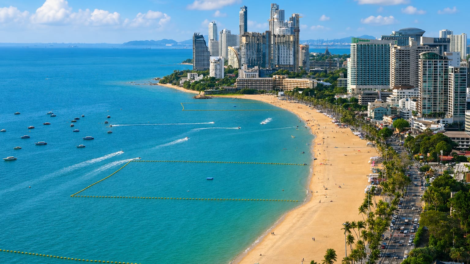 Pattaya Beach in daylight, a curving sandy bay lined with high-rise hotels and palms, boats on turquoise water.