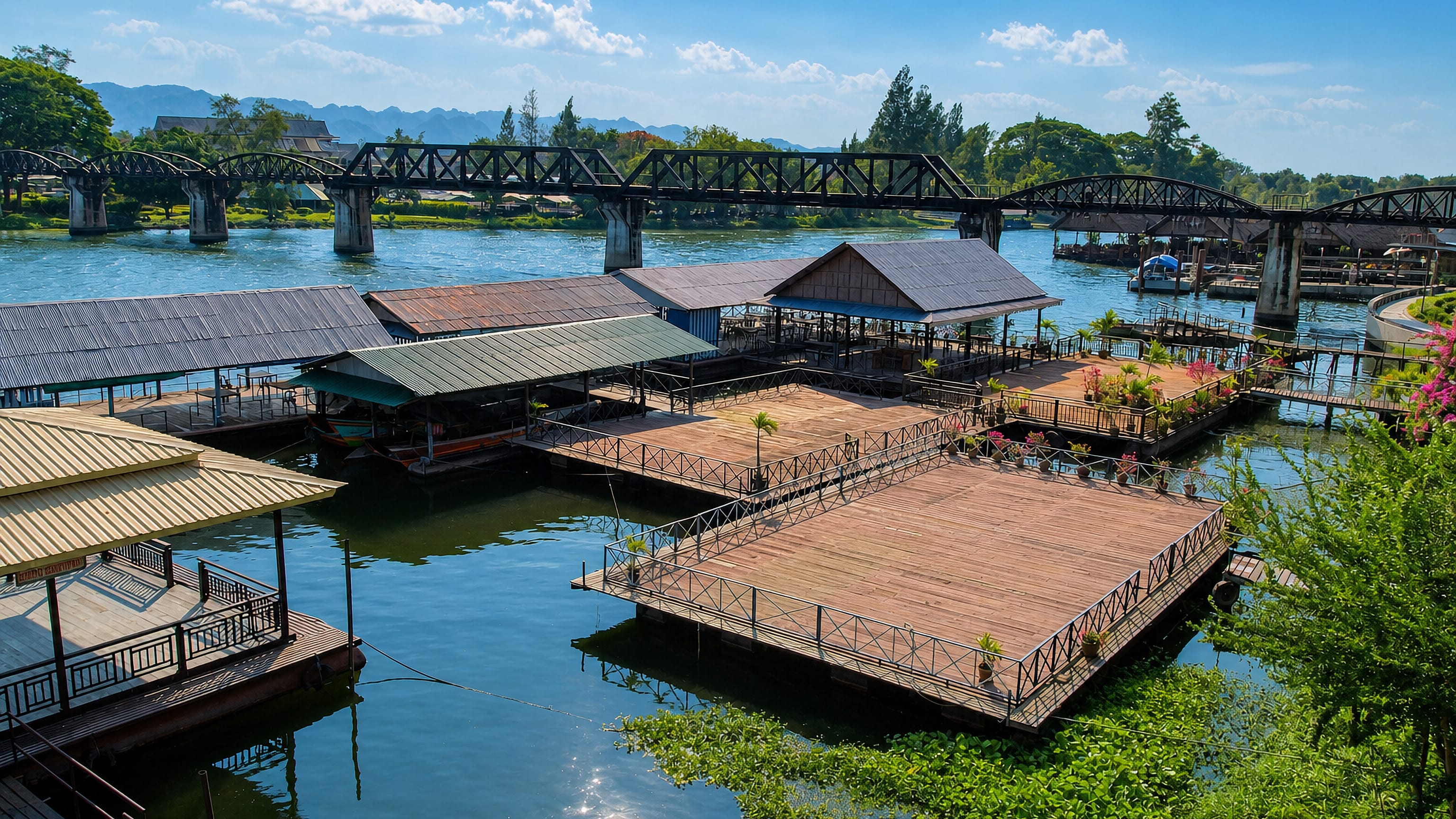 Bridge over the River Kwai spanning the water behind floating raft restaurants in Kanchanaburi, Thailand.