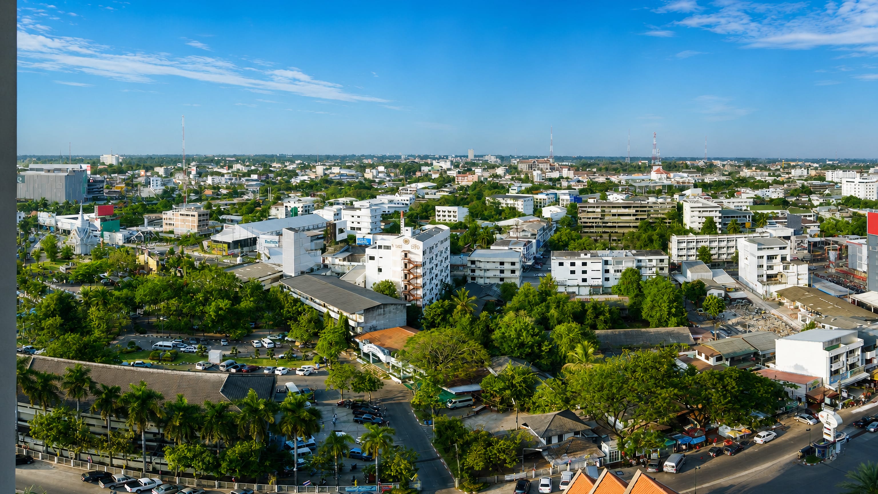 Aerial view over the low-rise centre of Khon Kaen, Thailand, with temple roofs and leafy streets.