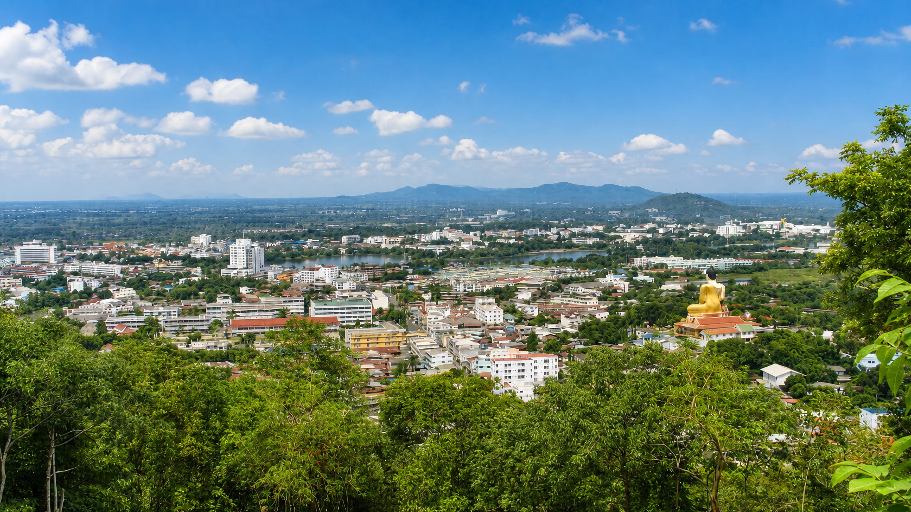 Hilltop view over Nakhon Sawan, Thailand, with a golden Buddha statue above the riverside town and green hills.