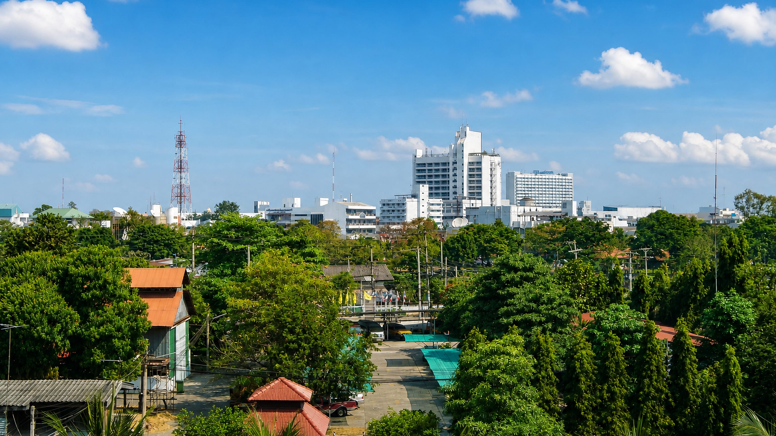 Leafy low-rise neighbourhoods and white mid-rise towers under a blue sky in Phitsanulok, Thailand.