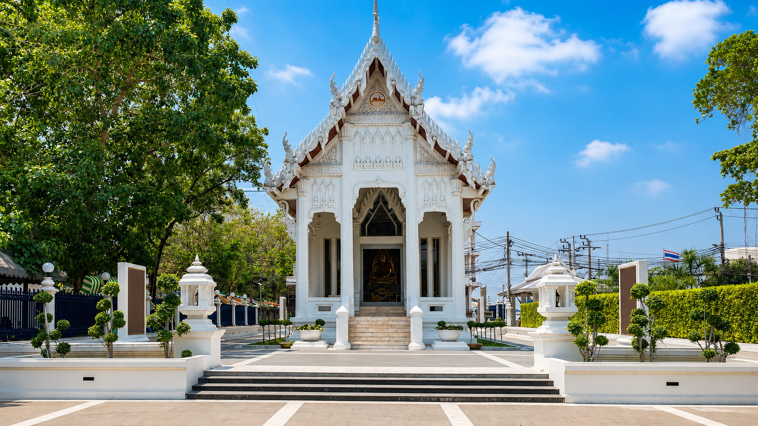A white Thai temple hall with gilded Buddha and tiered roof in Samut Prakan, Thailand.