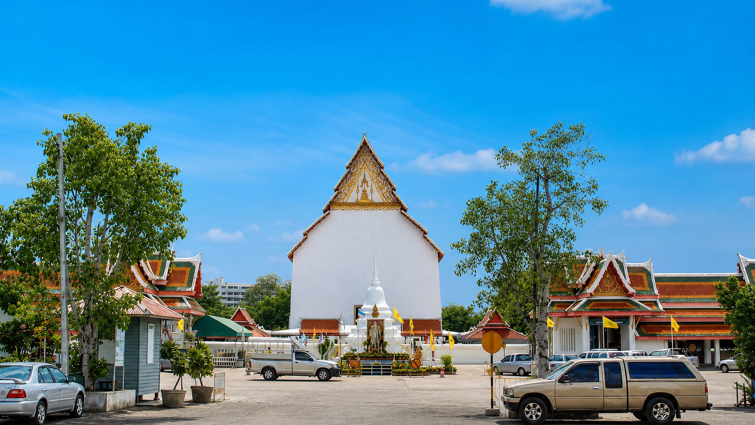 White temple hall, chedi and gilded Thai roofs at a wat courtyard in Suphan Buri.