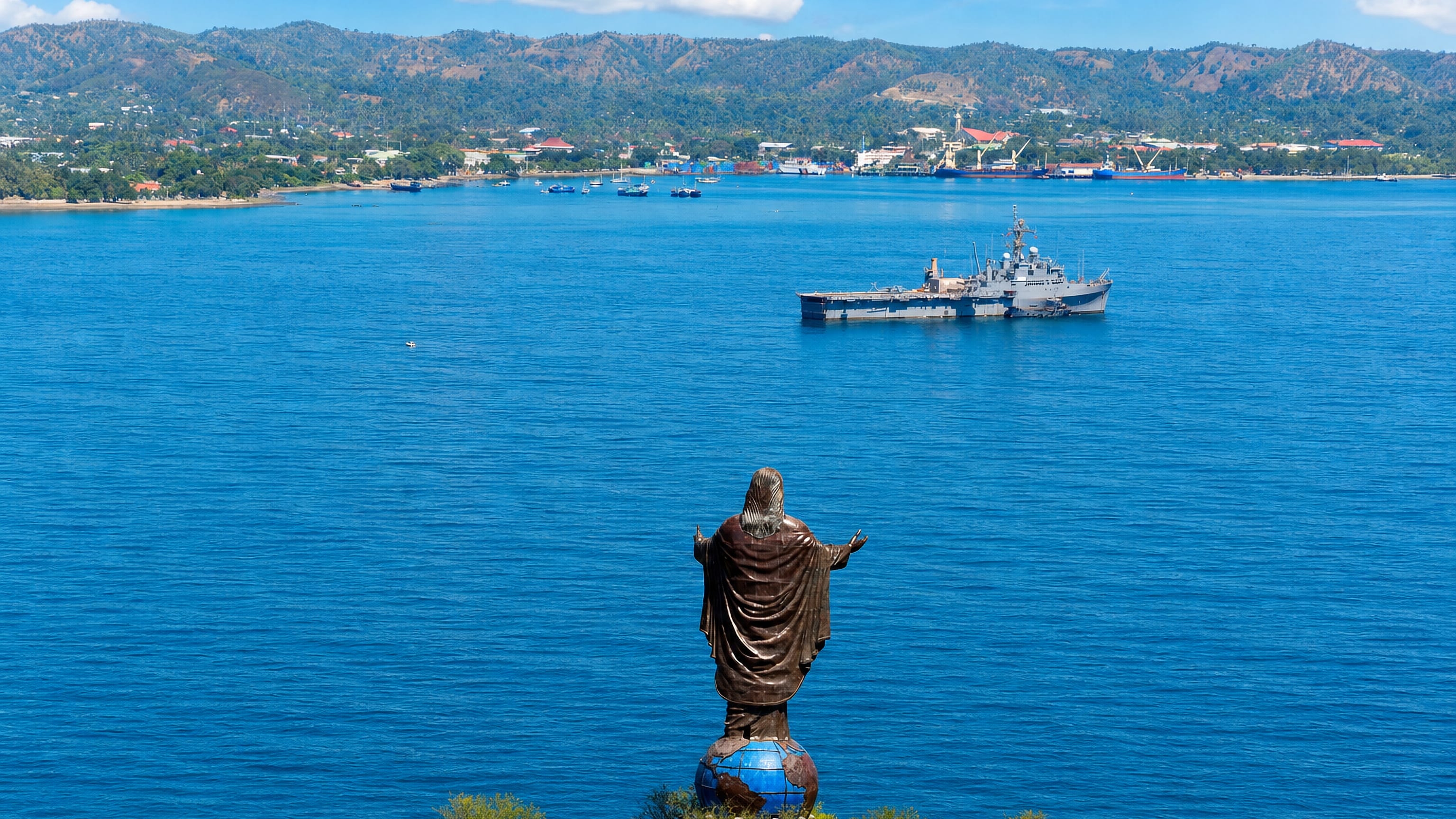 The Cristo Rei statue on its globe above Dili's harbour, with the city and green hills across the blue bay.