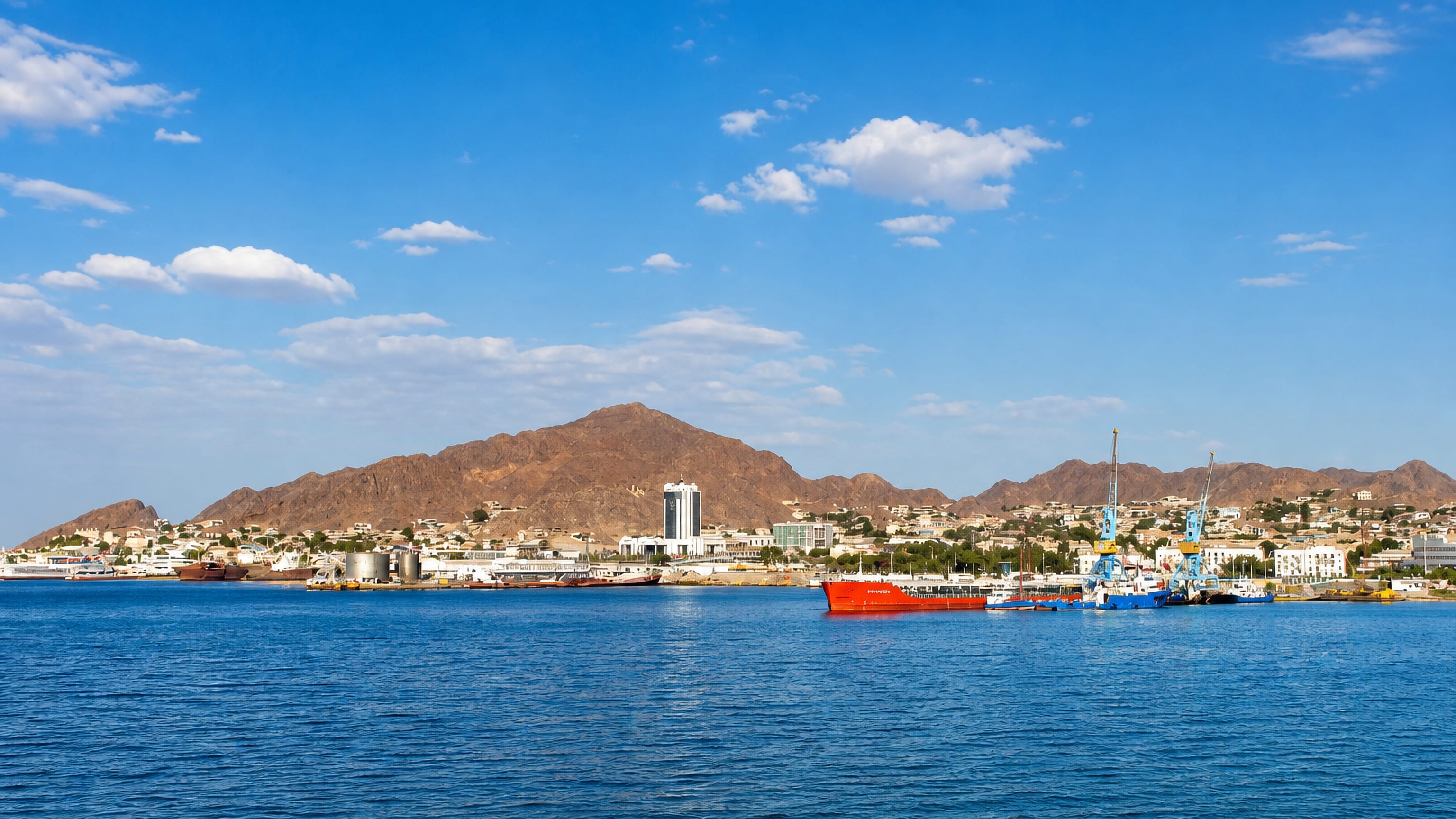 Cargo ships and harbour cranes at Turkmenbasy's Caspian port below bare brown mountains.